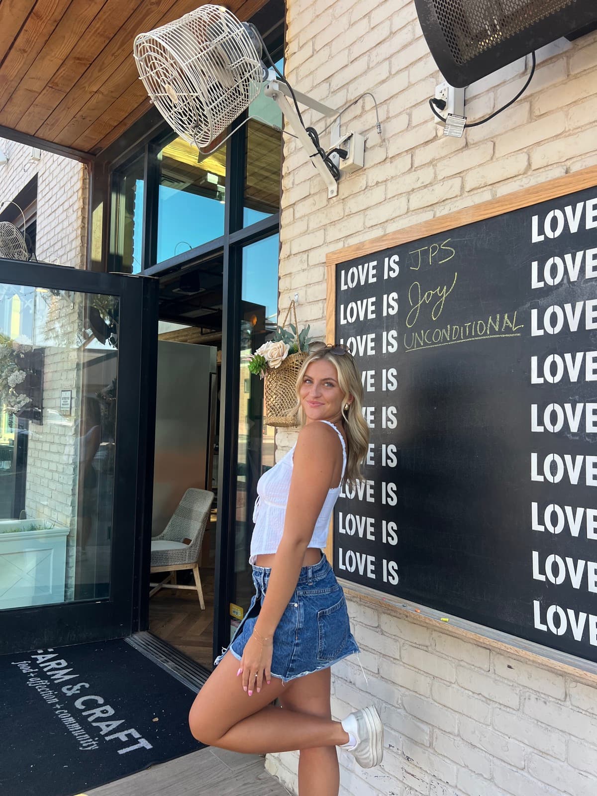 Devyn McCreery outside Farm & Craft, beside a chalkboard wall reading LOVE IS